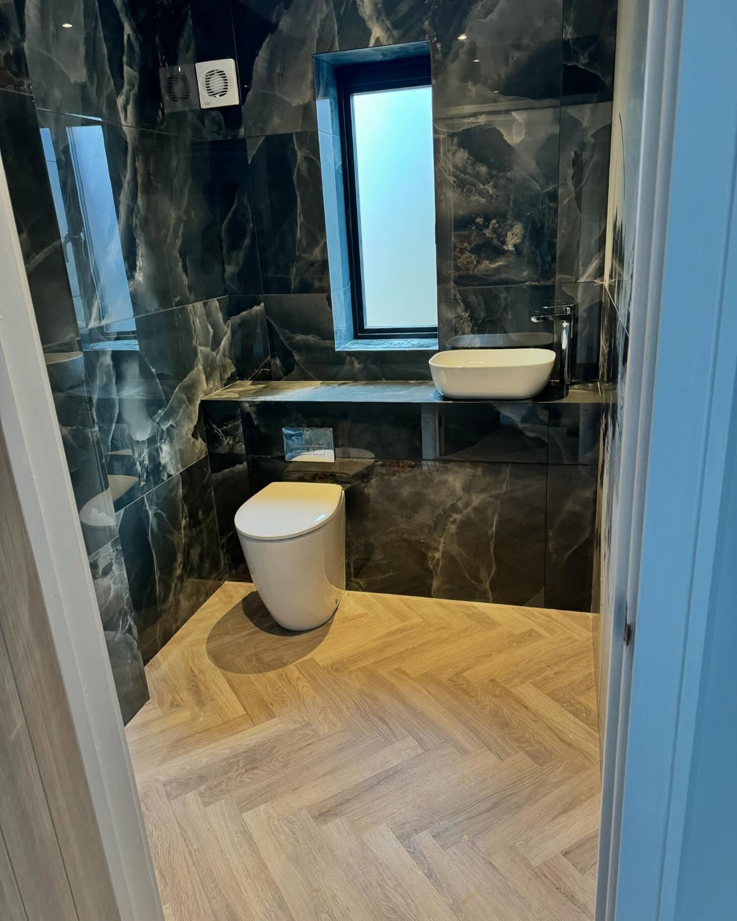 Cloakroom lined in dark marble-effect porcelain with herringbone floor