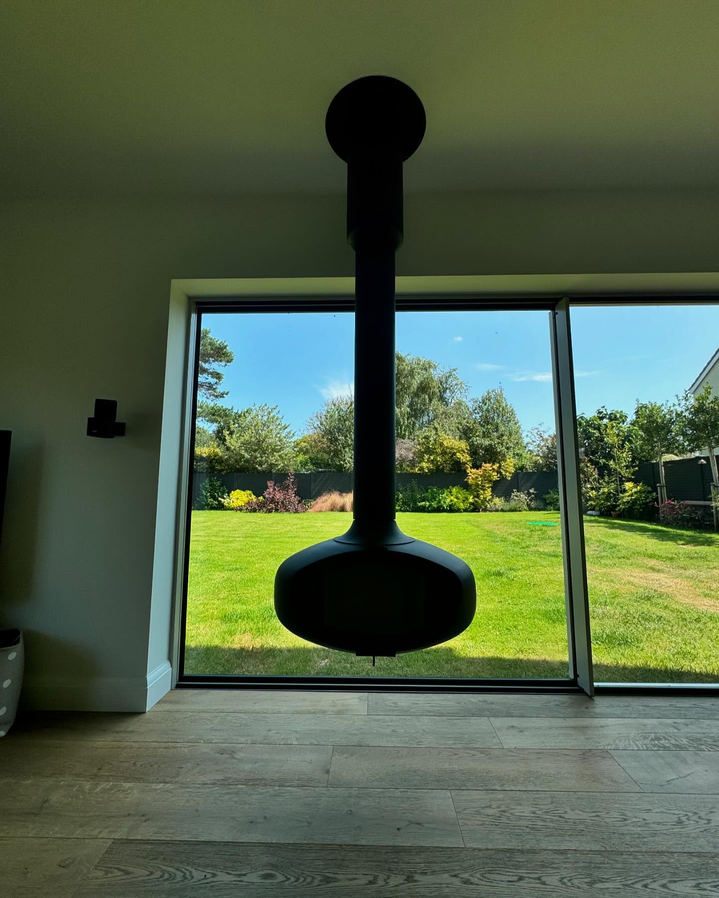 Suspended wood burning stove set against a full-height glazed opening