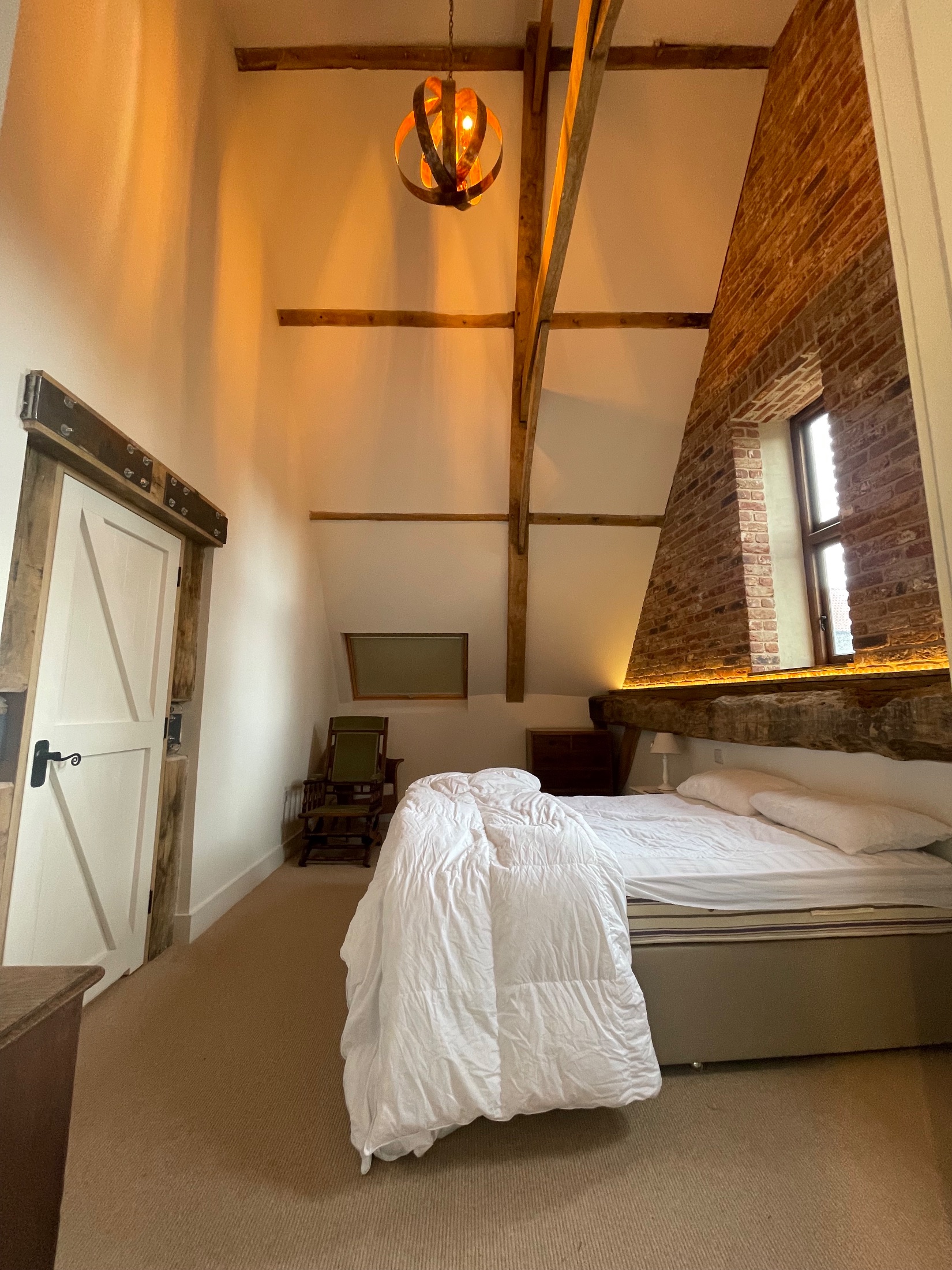 Barn conversion bedroom with exposed oak trusses and brick gable wall