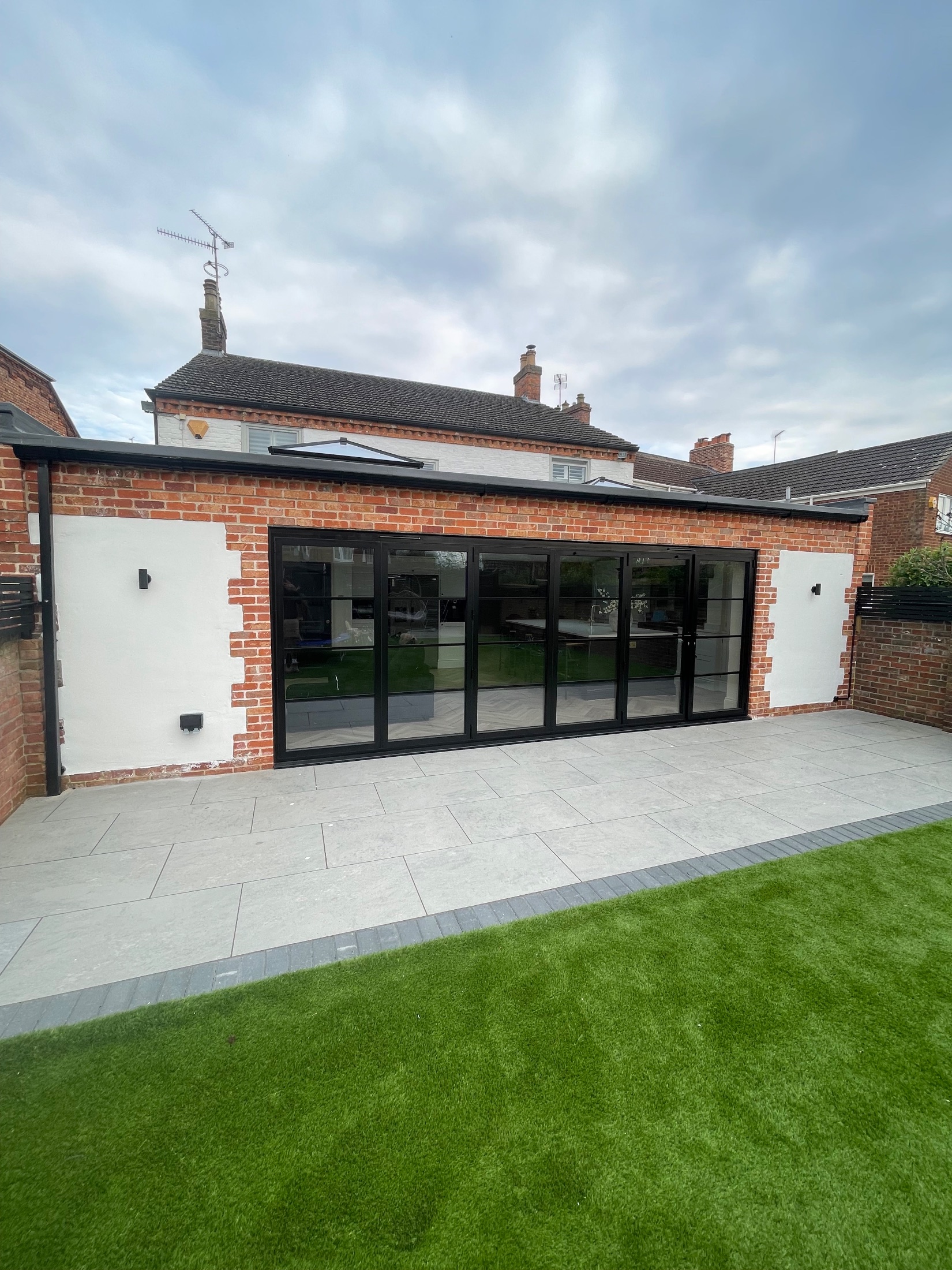 Brick garden room extension with black bifold doors open onto a porcelain terrace